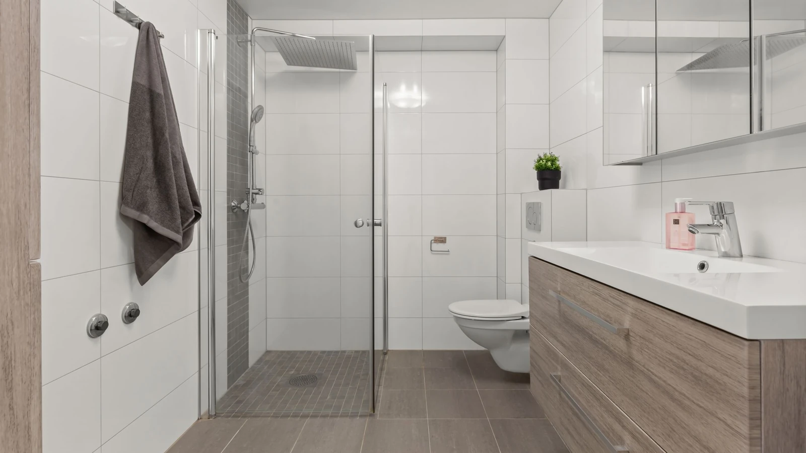Douche de plain-pied fermée par une porte vitrée, carrelage blanc aux murs et gris au sol